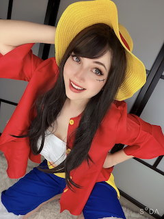 Woman wearing red jacket, yellow hat, and blue pants sitting on floor smiling