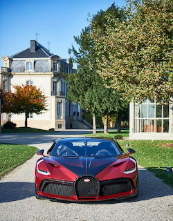 Red Bugatti Divo parked on a driveway in front of a large house and trees