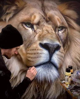 Artist in a black beanie painting a large realistic lion portrait