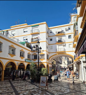 Sunlit cobblestone street in Torremolinos with white buildings, arches, balconies, and pedestrians