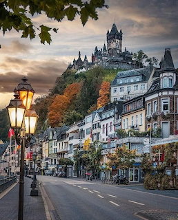 German town street with historic buildings and Cochem Castle on hiltop at dusk with autumn foliage