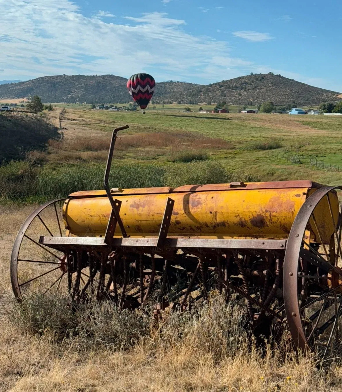 Hot air balloon floating over rural landscape with vintage yellow farm equipment in foreground