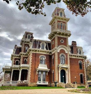 Historic red brick Victorian mansion with towers and ornate windows under a cloudy sky