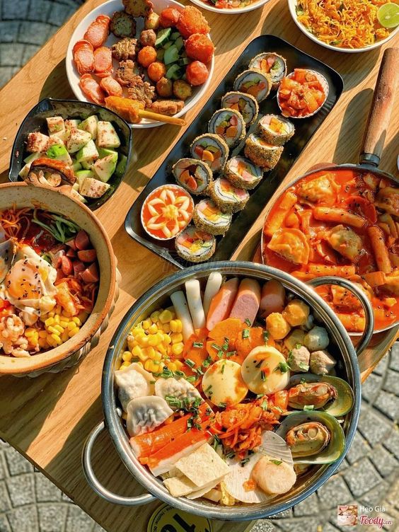 Overhead view of assorted Korean dishes and sushi arranged on a wooden table with chopsticks