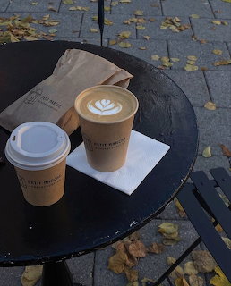 Two paper coffee cups on a round black outdoor table with autumn leaves on the ground