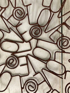 Brown metal wire sculptures with spiral and geometric shapes arranged together on a gray surface