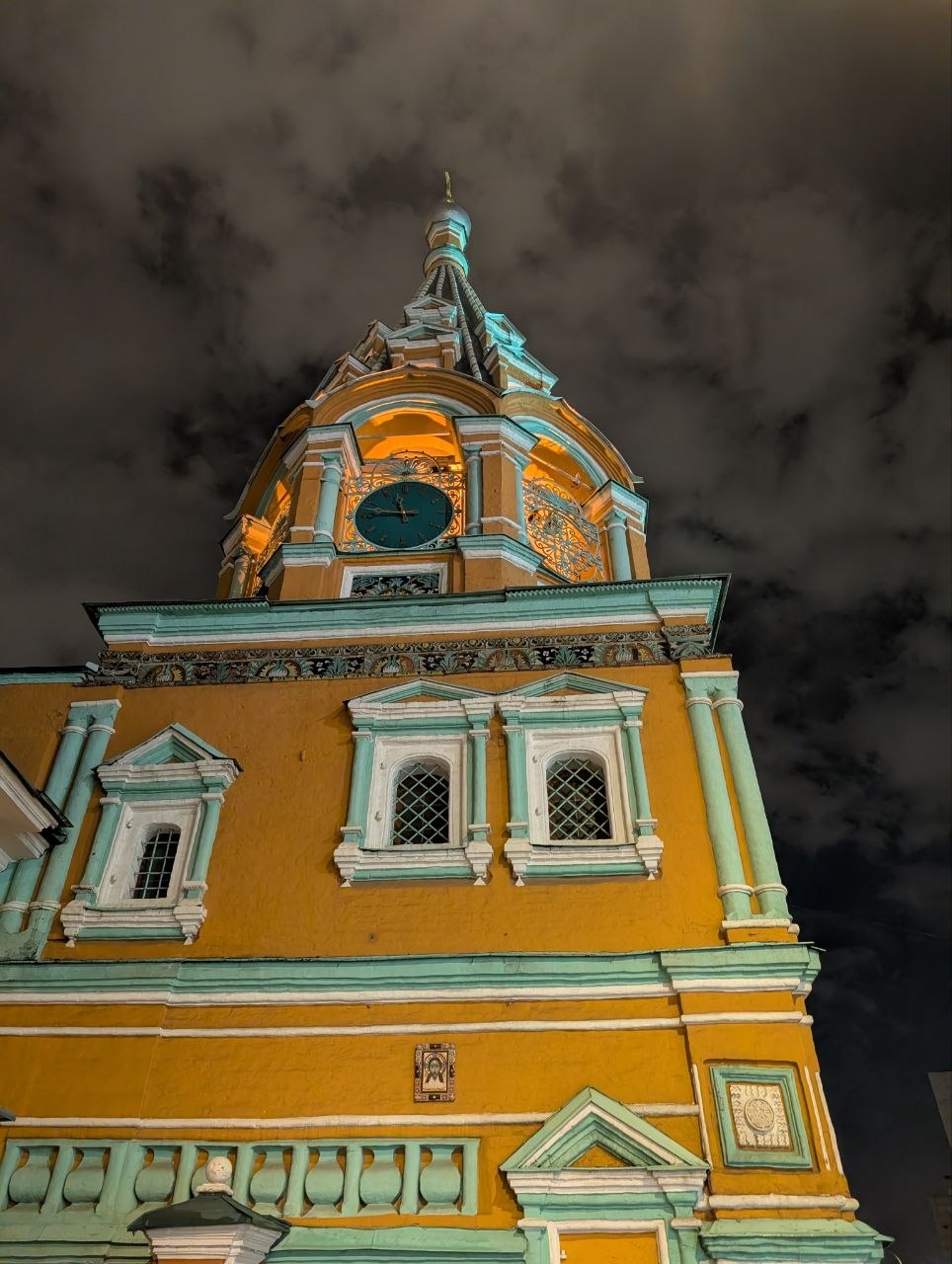 Yellow Orthodox church tower with green dome under dark stormy clouds