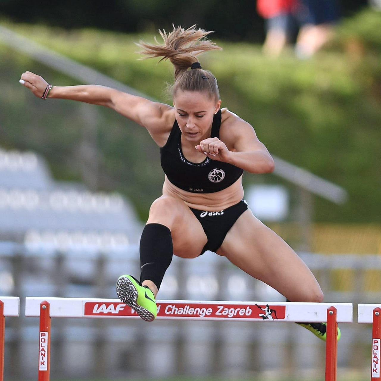 Female track athlete jumping over a hurdle on an outdoor running track