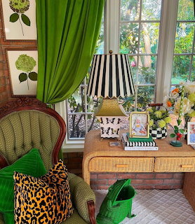 Cozy room corner with green armchair, striped lamp, flowers, and tall windows