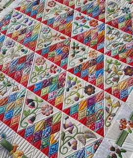 Colorful patchwork quilt with triangle patches, floral embroidery, and red borders on white background