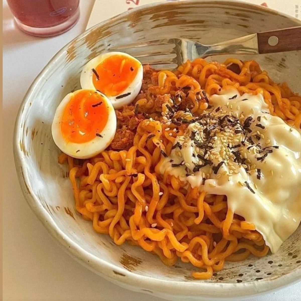 Bowl of spicy ramen noodles with melted cheese, ground meat, and two soft-boiled egg halves