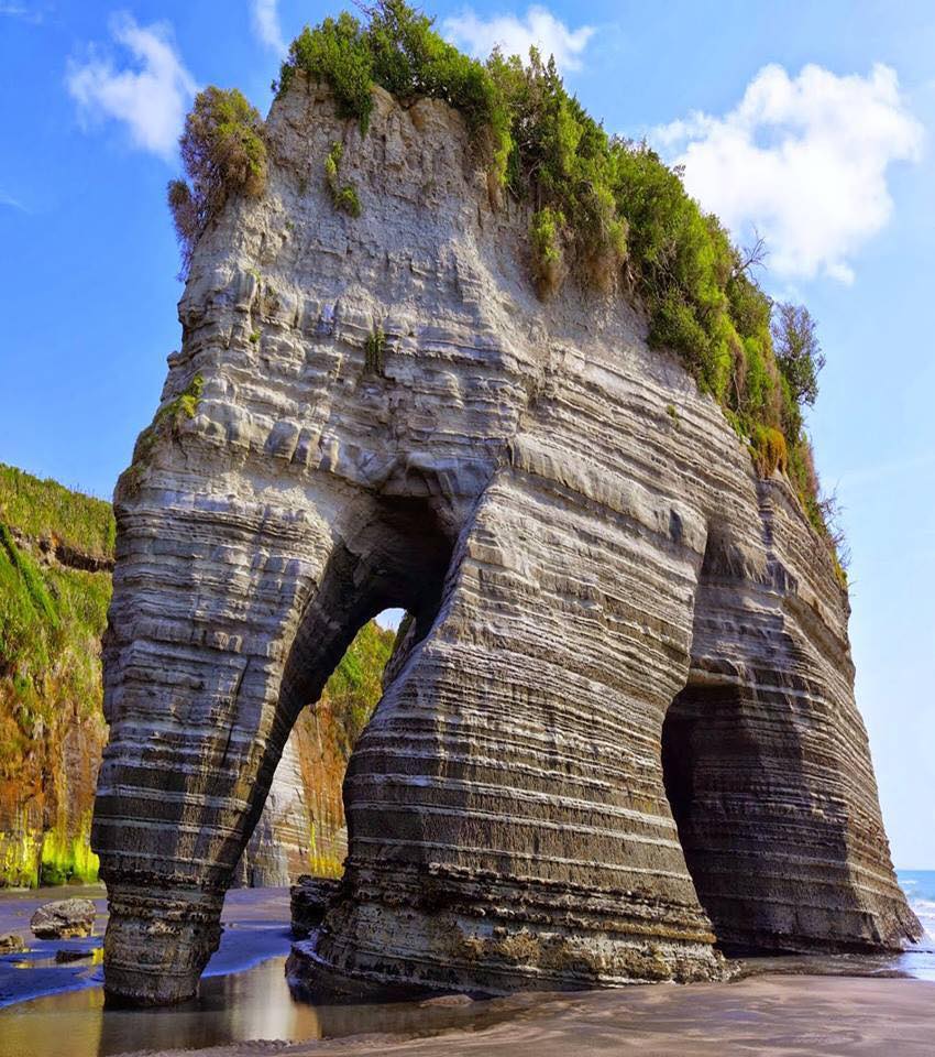 Layered coastal rock arch on a beach beneath a blue sky