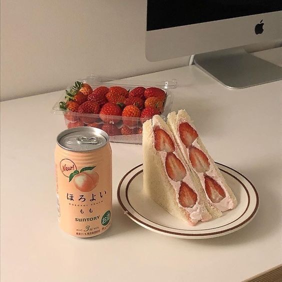 Strawberry sandwich with cream on plate next to peach drink and container of fresh strawberries