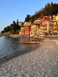 Pebble beach at Lake Como with colorful hillside village buildings beside calm water