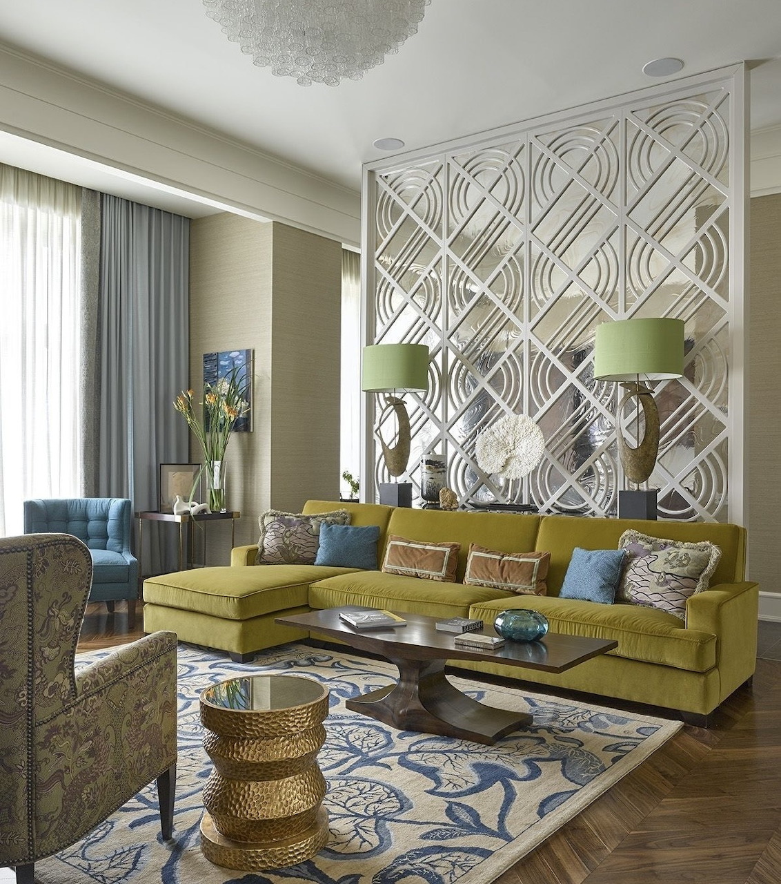 Modern living room with olive-green sectional sofa, white geometric room divider, patterned rug, and colorful accent chairs