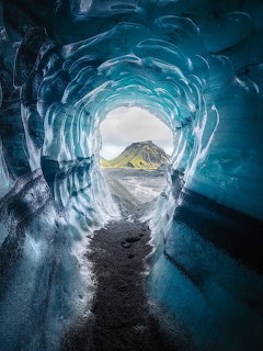Blue glacial ice cave tunnel with mountain view at exit in Iceland