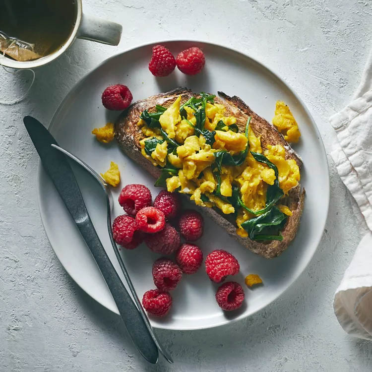 Scrambled eggs on toast with raspberries and coffee on white plate