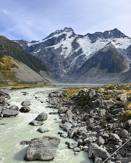 Glacial river with rocks flowing through valley below snow-covered Mount Cook mountain range