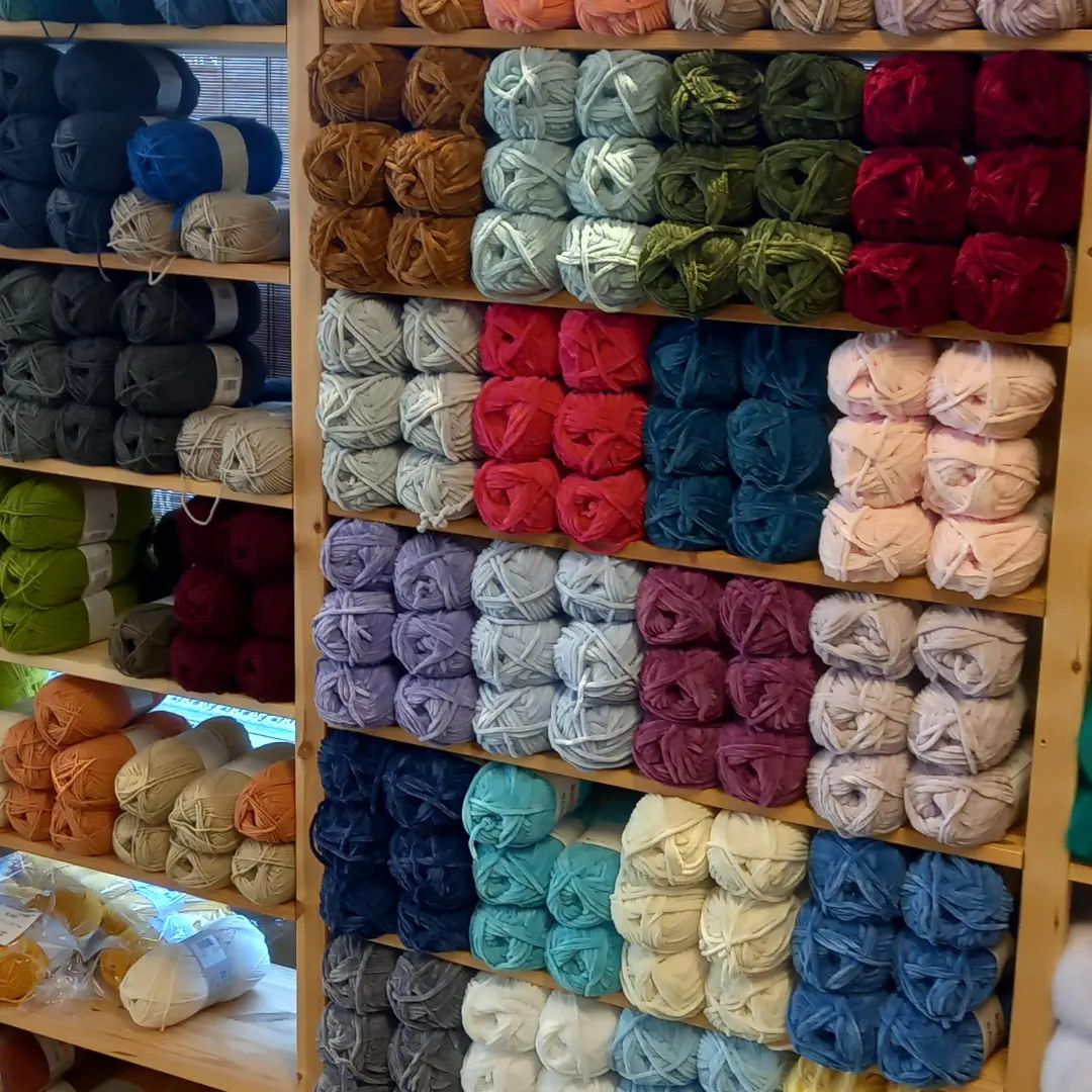 Wooden shelves stocked with colorful yarn balls arranged in rows by color