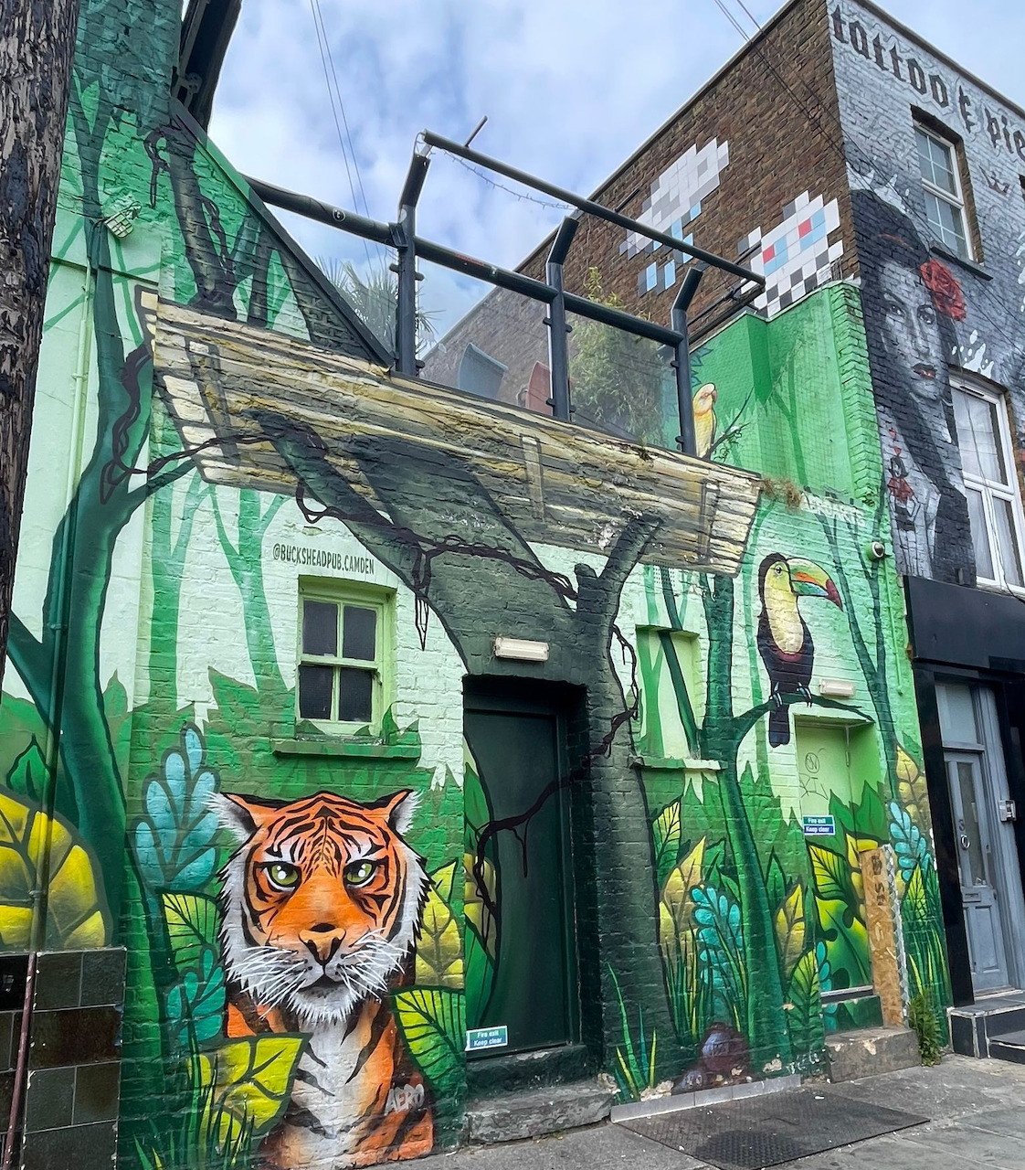Colorful street art mural of a tiger in green jungle foliage on a building with CAMDEN lettering