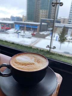 Black cup of latte on a table by a window with a snowy city view outside