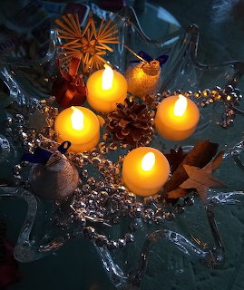 Four lit candles arranged with pine cones and greenery on decorative glass star tray