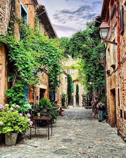 Coblestone street in Peratallada Spain with ivy-covered stone walls, poted flowers, and café tables