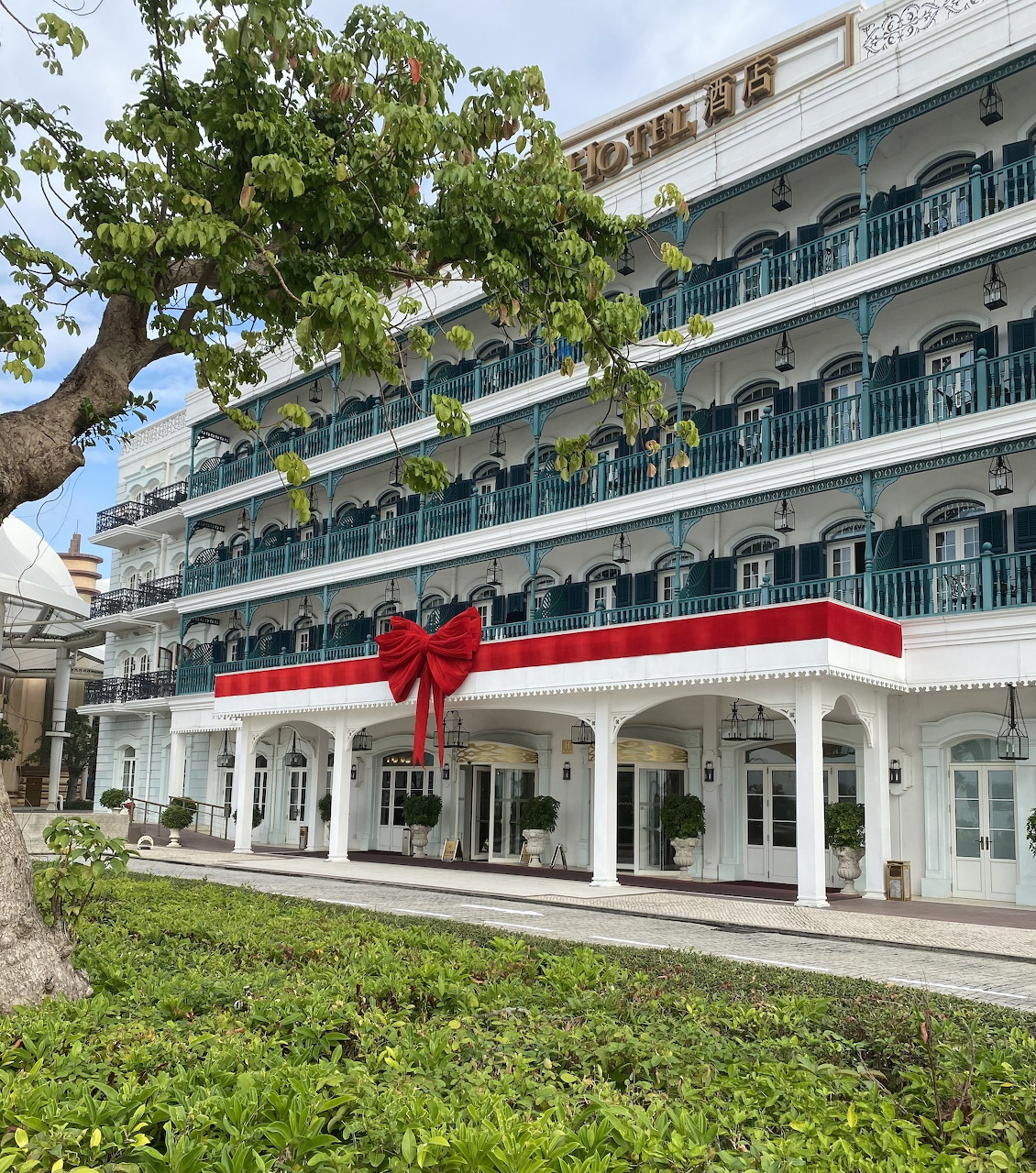 Rocks Hotel Macao, white colonial building with teal balconies and a large red bow at the entrance