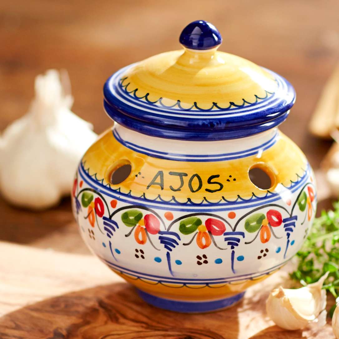Decorative ceramic garlic jar with yellow lid and hand-painted floral pattern on wooden surface