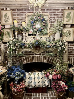 Brick fireplace mantel covered with flowers, greenery, and framed botanical prints indoors