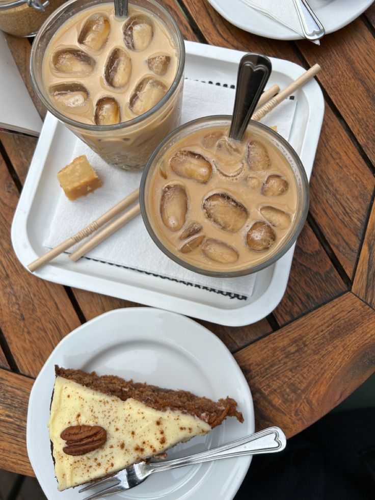Two iced coffees with decorative foam art and a slice of carrot cake on a white serving tray