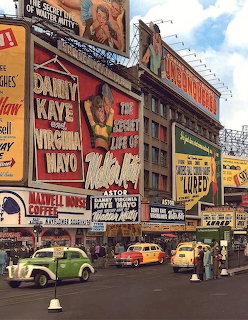 Vintage city street with theater billboards, storefront signs, and classic cars