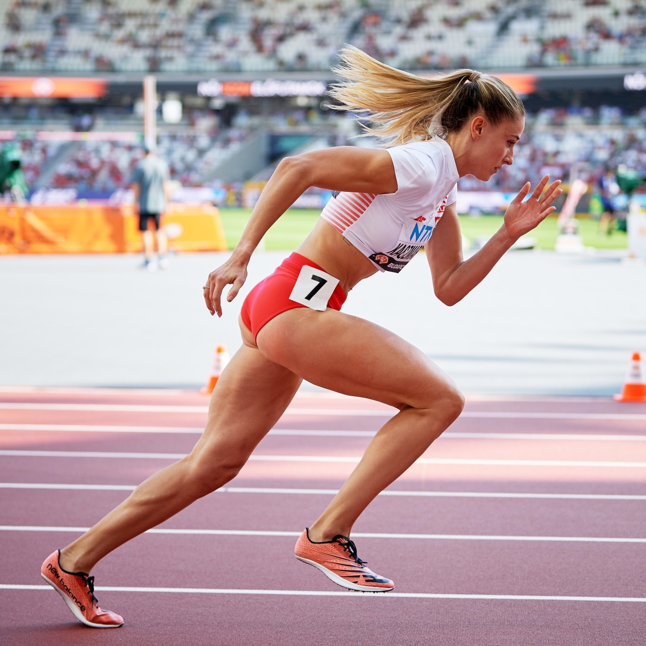 Female track athlete powerfully sprinting from starting blocks on purple running track in packed stadium