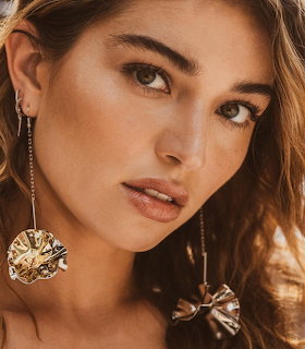 Close-up of a woman with brown hair and green eyes wearing large gold earrings