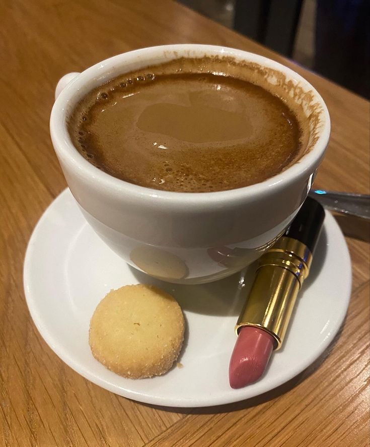 White cup of hot coffee on saucer with a butter cookie and pink lipstick on a wooden café table