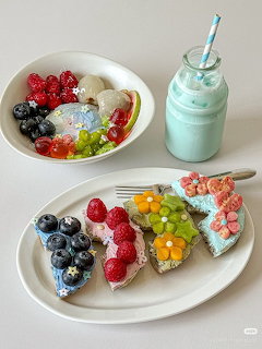 Four slices of toast with colorful fruit toppings next to a bowl of berries and a blue smoothie bottle