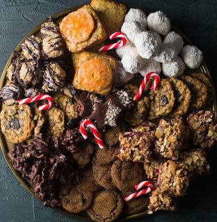 Round tray of assorted cookies, bars, powdered sweets, and mini candy canes on a dark surface