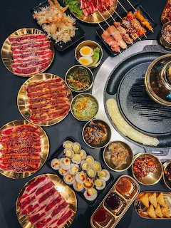 Overhead view of Korean BBQ table with meat platters, grill, and assorted side dishes