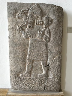 Ancient Mesopotamian stone relief showing carved bearded figure with ceremonial objects