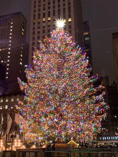 Large lit Christmas tree at Rockefeller Center at night with city buildings in background
