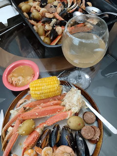 Plate of seafood boil with crab legs, mussels, corn, sausage, potatoes, and a glass of white wine