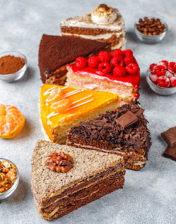 Five different layered cake slices arranged in a row with various toppings and decorative ingredients around them