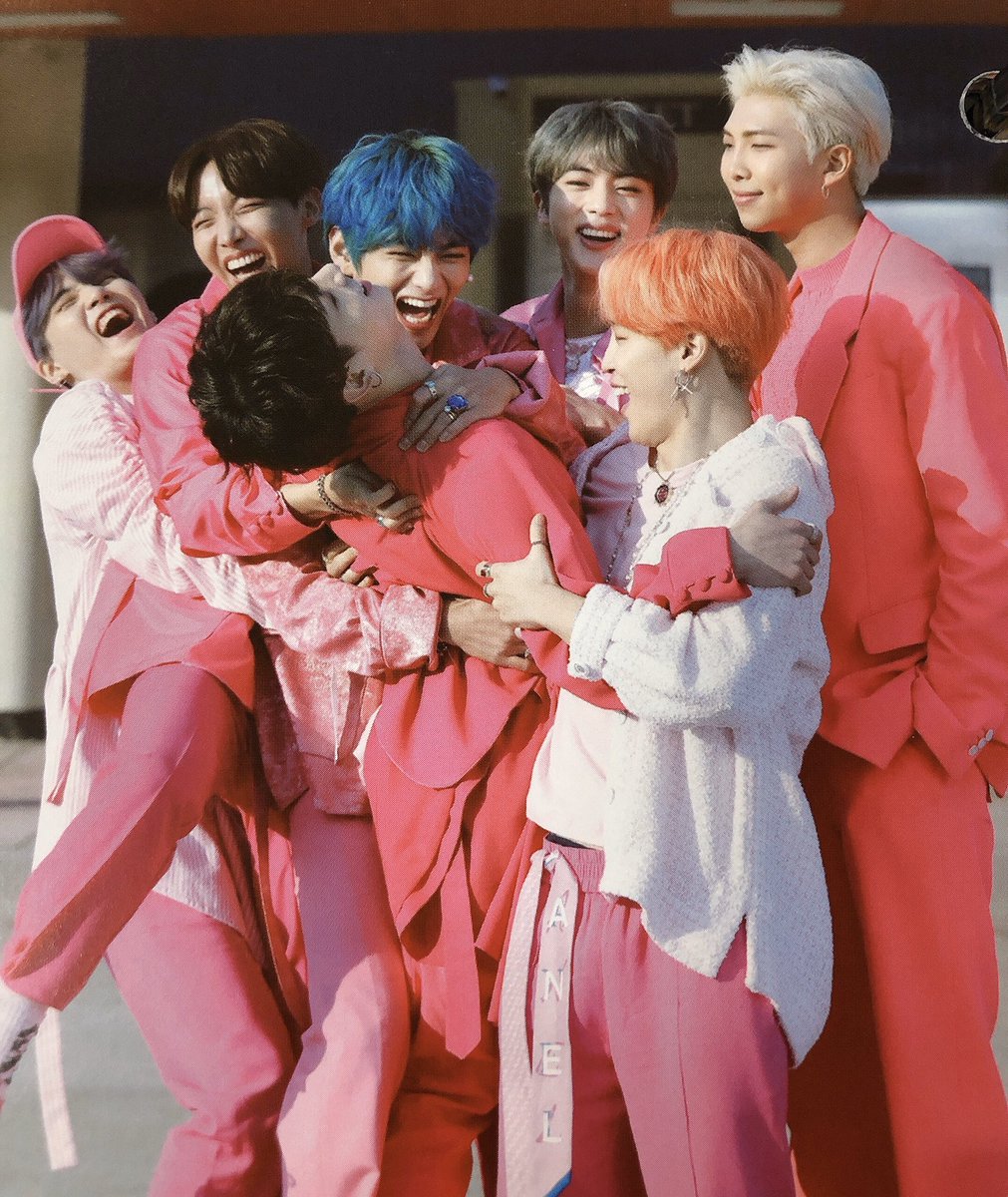 BTS members in colorful pink, red and white suits posing together in a happy group photo