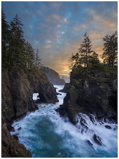 Rocky coastal cliffs with crashing waves and pine trees silhouetted against a sunset sky on the Oregon coast