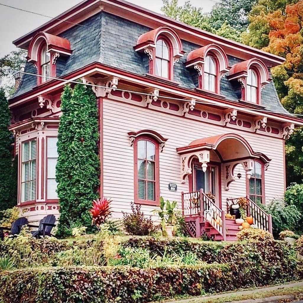 Pink Victorian house with red trim, Mansard roof, ivy entrance, and fall trees