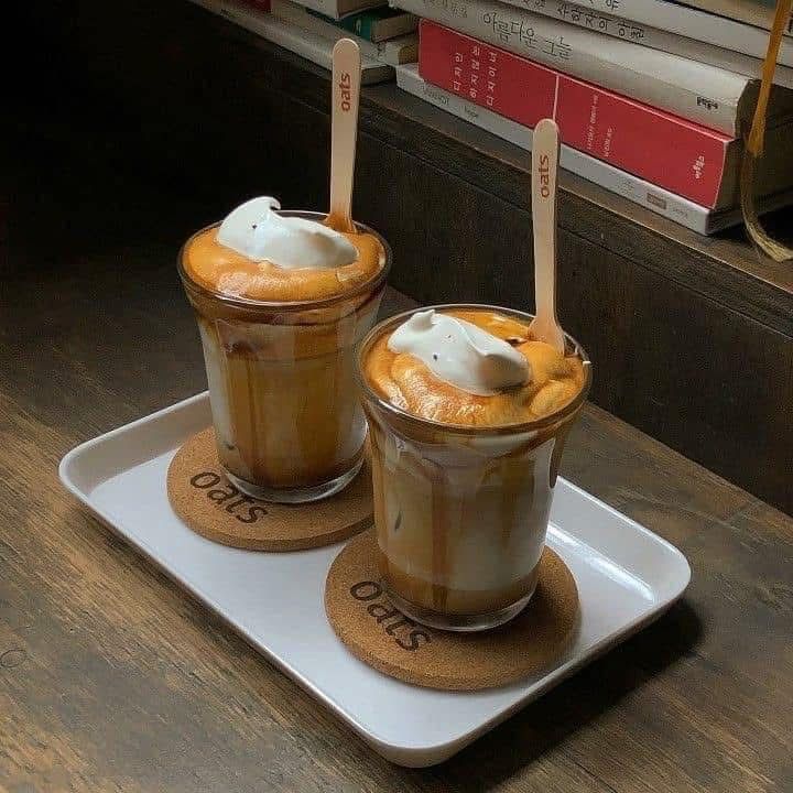 Two layered coffee drinks with creamy foam tops on a tray beside books
