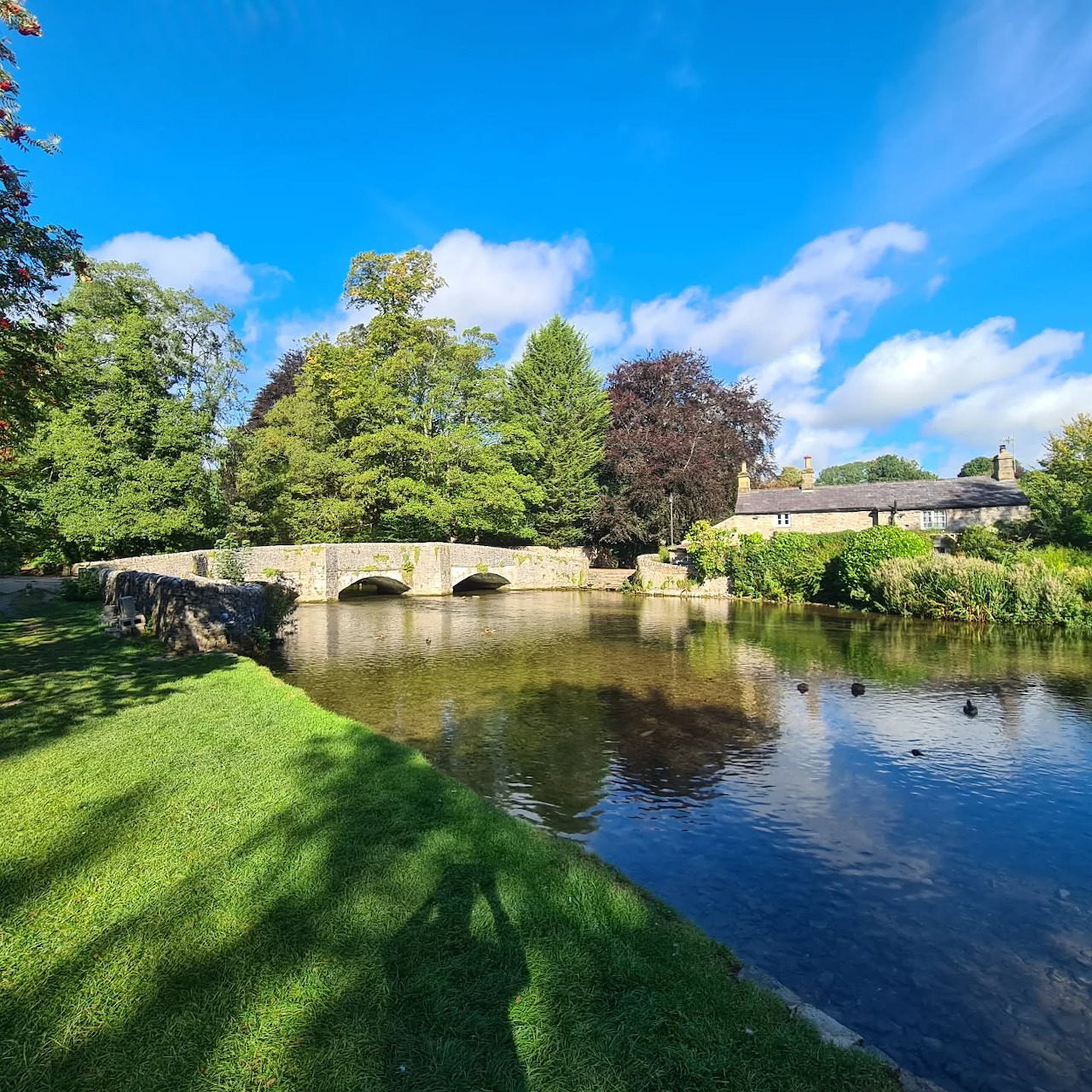 Historic stone bridge spanning a river with green lawns and trees on a sunny day