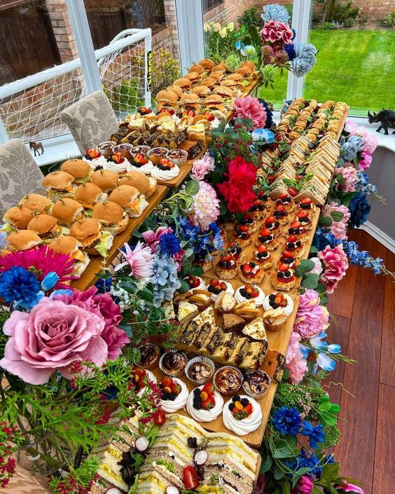 Long table laden with variety of desserts and colorful flower arrangements on outdoor patio