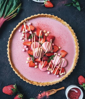 Pink strawberry tart topped with fresh strawberries, white chocolate drizzle, and candy pearls on dark surface