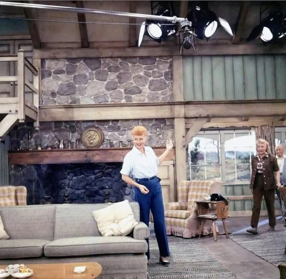 Vintage TV studio set with a rustic living room, stone fireplace, sofa, and two people
